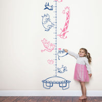 Height chart wall sticker with animals on a trampoline with a young girl nearby.