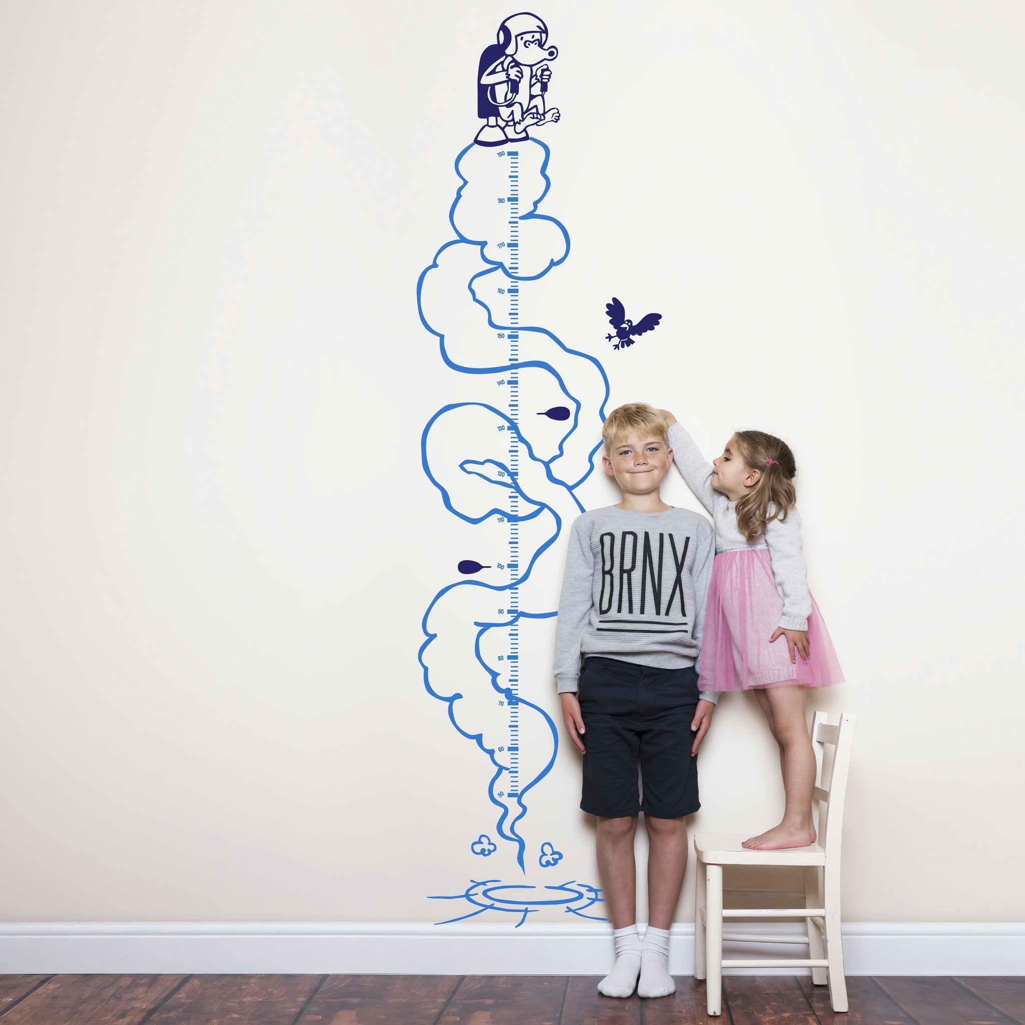 Height chart wall sticker of a monkey with a jetpack with a young boy and girl nearby.