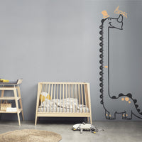 Height chart wall sticker of a long necked dianosaur in a nursery with a crib.