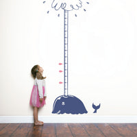 Height chart wall sticker of a whale blowing water from its blow-hole with a young girl nearby.
