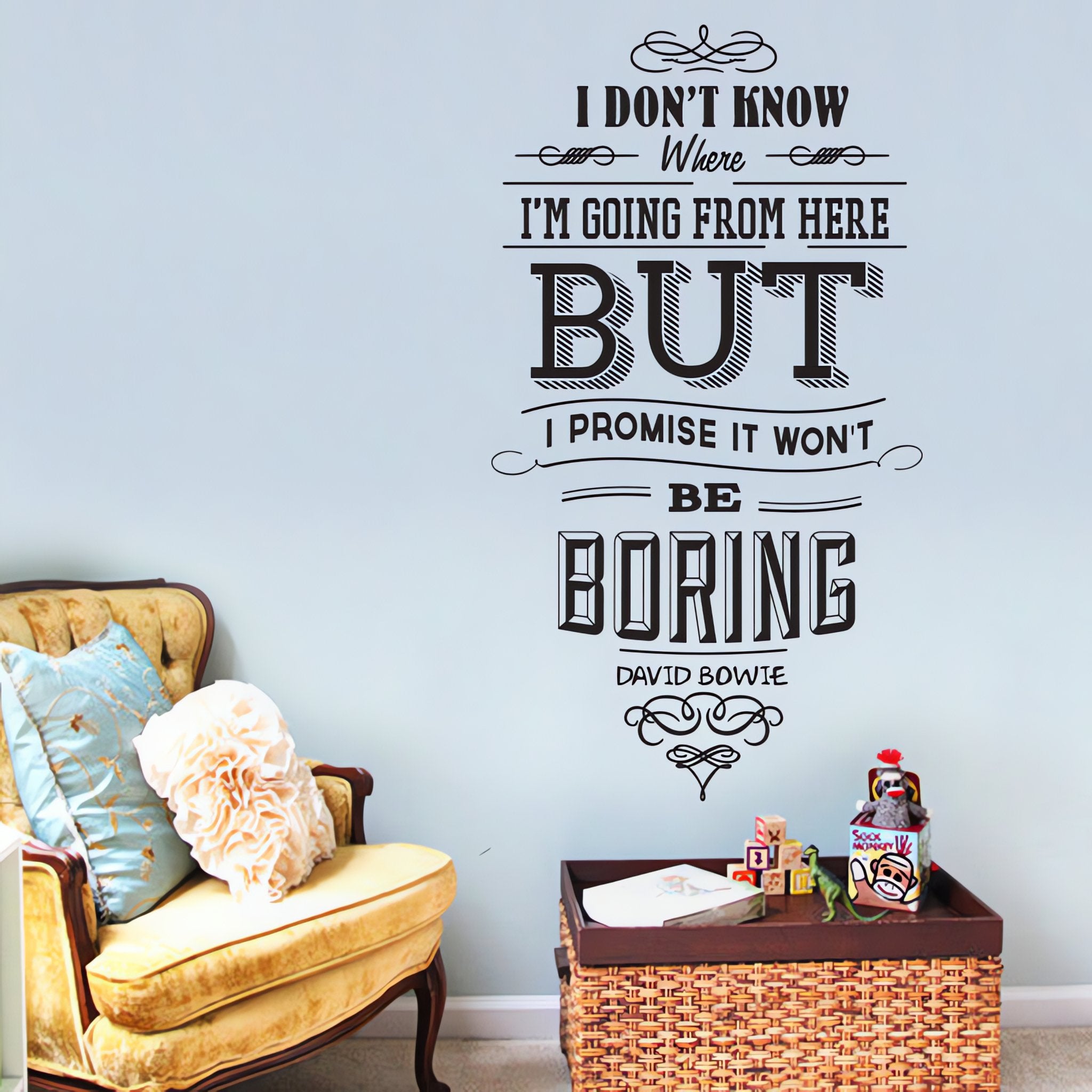 Wall quote sticker with text "I Don't Know Where I Am Going From Here But I Promise It Won't Be Boring" in a living room with a chair and table.