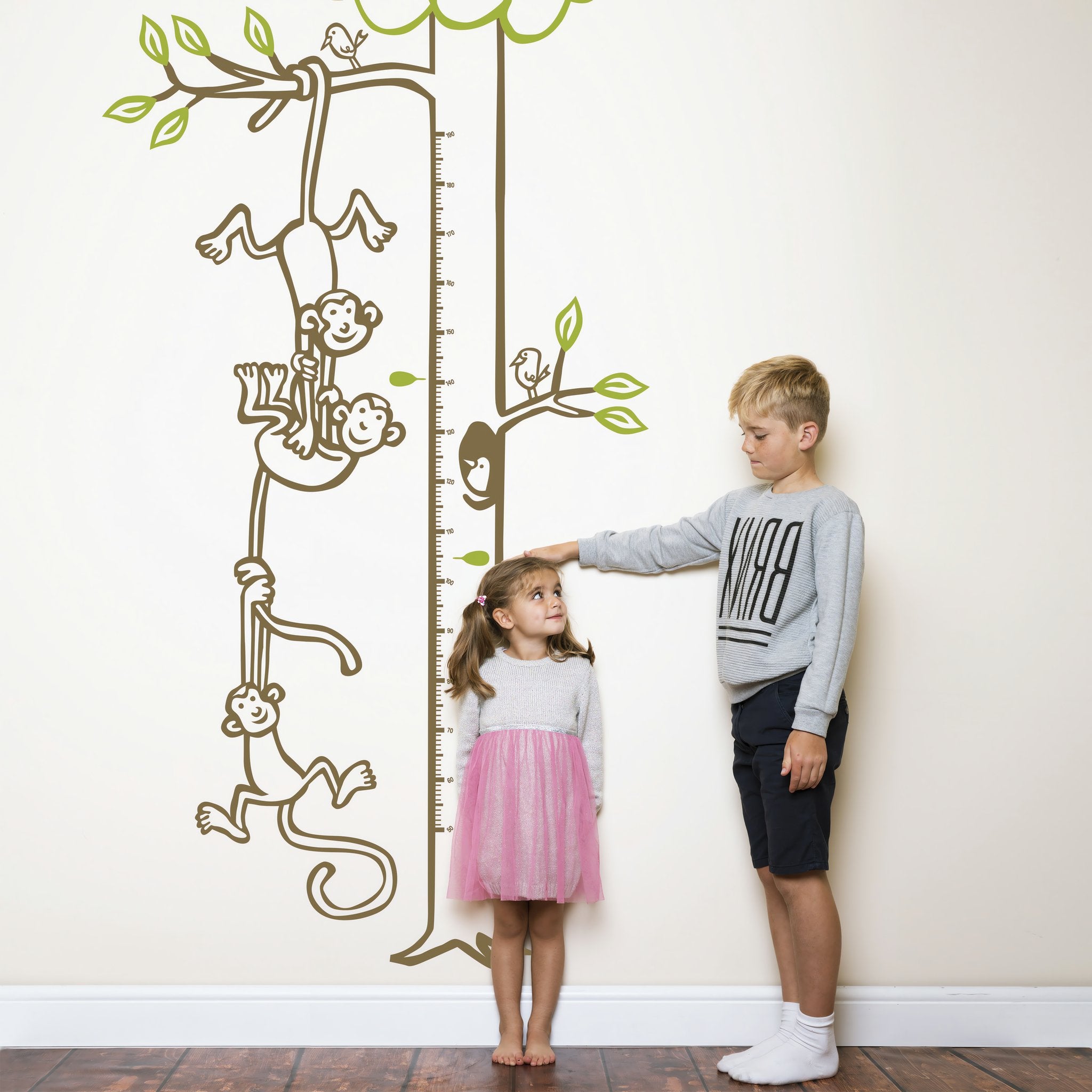 Height chart wall sticker with monkeys hanging from a tree to form a chain with a young boy and girl nearby.