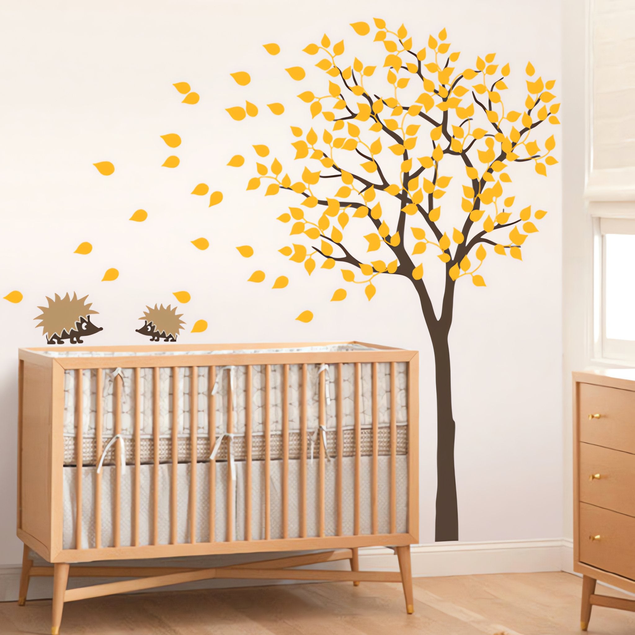Tree wall sticker with leaves blowing and hedgehogs playing in a nursery with a crib.