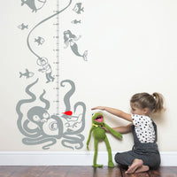 Height chart wall sticker with a boat and undersea monsters beneath the surface with a young girl playing with kermit nearby.