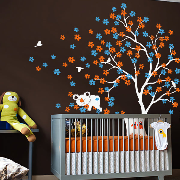 Tree wall sticker with a koala bear and birds in a nursery with a crib and stuffed toys.