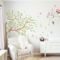 Tree wall sticker with birds and leaves blowing in a brightly lit room with chairs and a dresser.