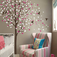 Tree wall sticker with blowing leaves and birds in a nursery with a crib and an armchair.