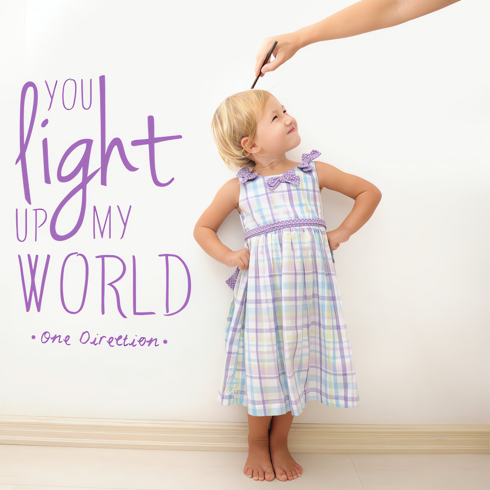 Wall quote sticker with text "You Light Up My World" by One Direction next to a happy little girl.