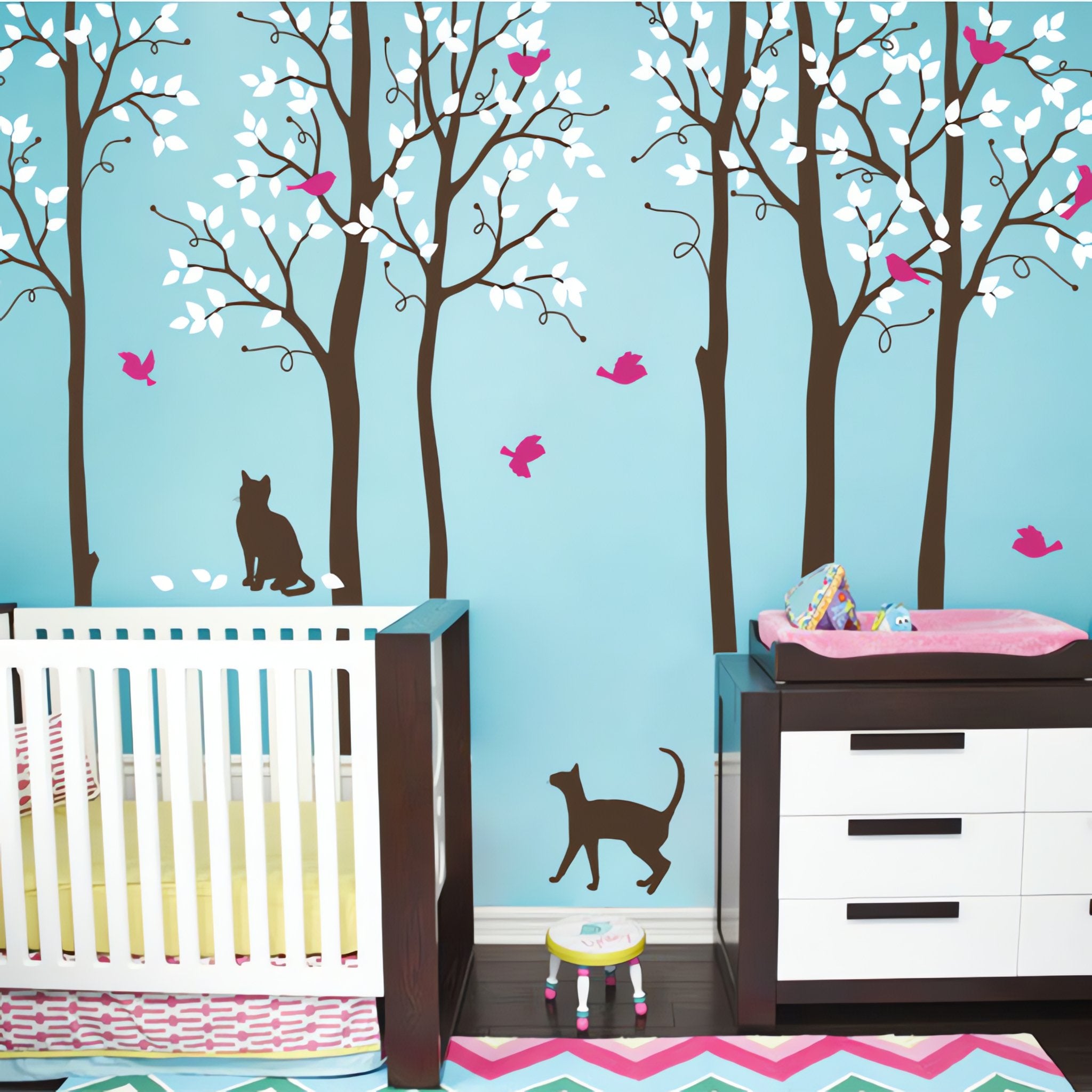Tree wall sticker with 2 cats and some birds in a nursery with a crib and a dresser.