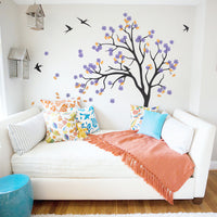 Wall tree sticker with leaves blowing and birds in a living room or bedroom with birdcages and a couch.