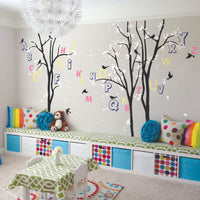 Tree wall sticker with leaves and  letters of the alphabet hanging from branches and birds in a nursery with a child sized table and a hanging light.