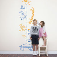 Height chart wall sticker with animals on a trampoline with a young boy and girl nearby.
