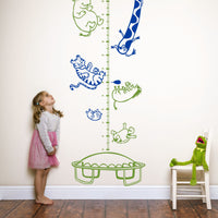 Height chart wall sticker with animals on a trampoline with a young girl nearby and kermit the frog sitting on a chair.