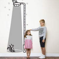 Height chart wall sticker of a cat bathed in light from a street lamp with a young boy and girl nearby.