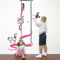 Height chart wall sticker of rupunzel in a tower being rescued py a prince with a young girl sitting on the floor and a boy pointing.