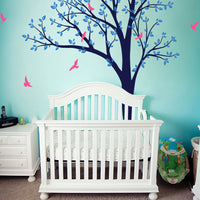 Tree wall sticker with birds in a nursery with a cot and a dresser.