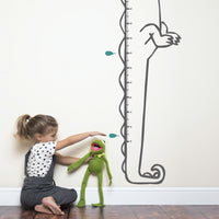 Height chart wall sticker of a cartoon crocodile with a young girl playing with kermit the frog toy.