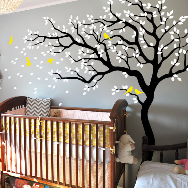 Tree wall sticker with leaves blowing and birds in a nursery with a crib.