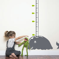 Height chart wall sticker of a whale blowing water from its blow-hole with a young girl playing with a kermit the frog toy.