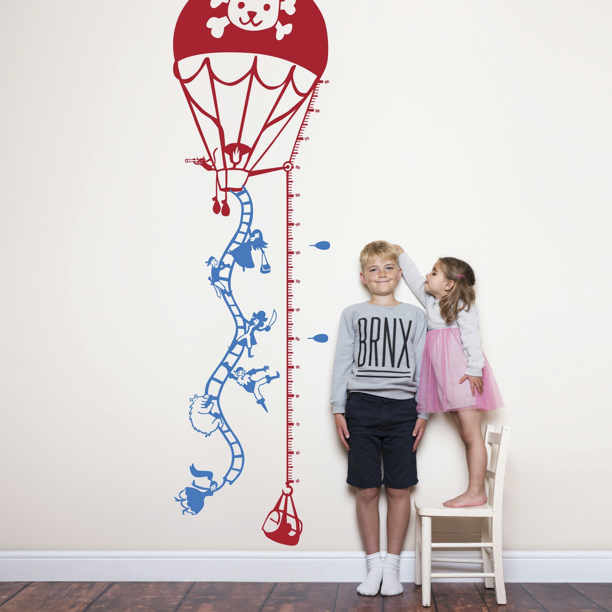 Height chart wall sticker of a hot air balloon taking off with a young boy and girl nearby.