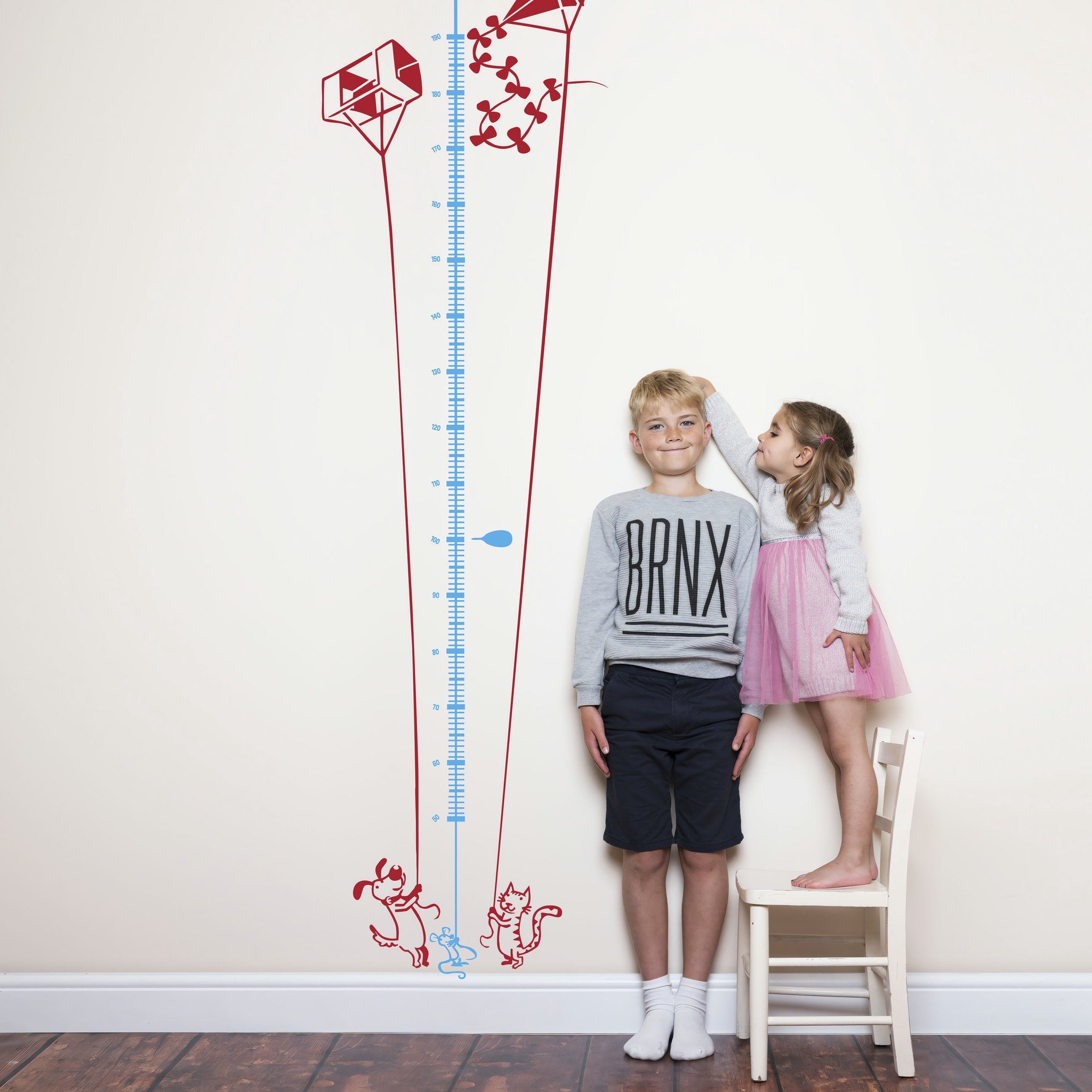 Height chart wall sticker of a kite being flown by a cat and dog with a young boy and girl nearby.