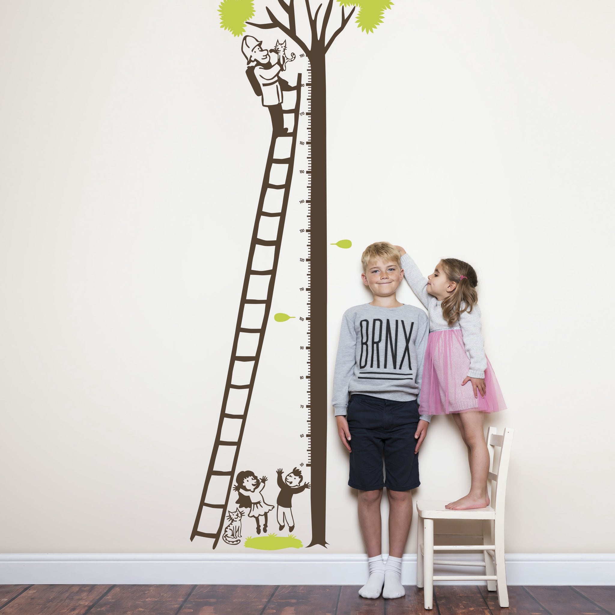 Height chart wall sticker of a kitten being rescued from a tree with a young boy and girl nearby.