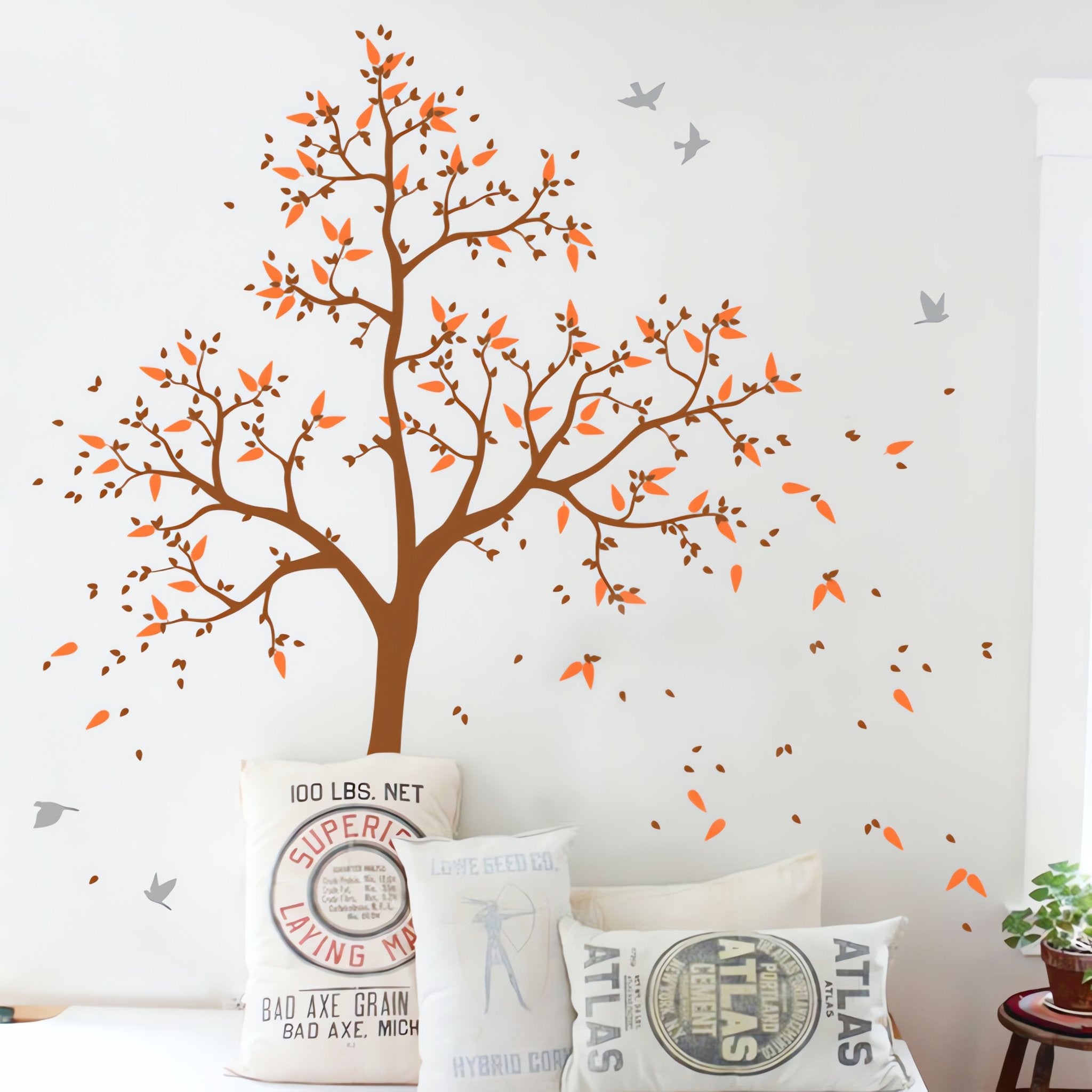 Tree wall sticker with leaves blowing, birds and a child's name above seating with cushions.