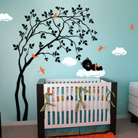 Tree wall sticker with a leaning tree, bears resting on clouds and birds in a nursery with a crib.