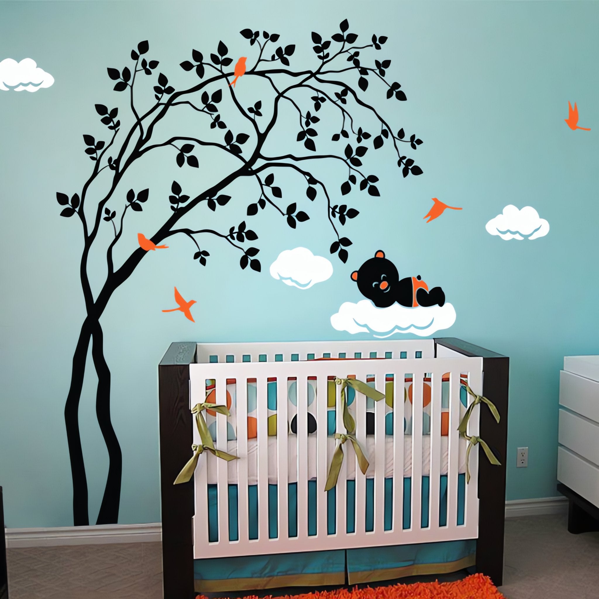Tree wall sticker with a leaning tree, bears resting on clouds and birds in a nursery with a crib.