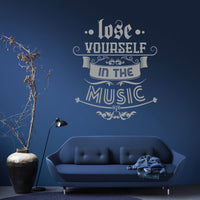 Wall quote sticker with text "Lose Yourself In The Music" in a living room with a couch, plant pot and a lamp.