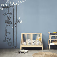 Height chart wall sticker with monkeys hanging from a tree to form a chain in a nursery with a crib.