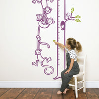 Height chart wall sticker with monkeys hanging from a tree to form a chain with a young girl sitting on a chair pointing.
