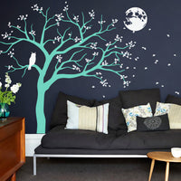 Tree wall sticker with a night time theme, owl and moon in a living room with a sofa and table.