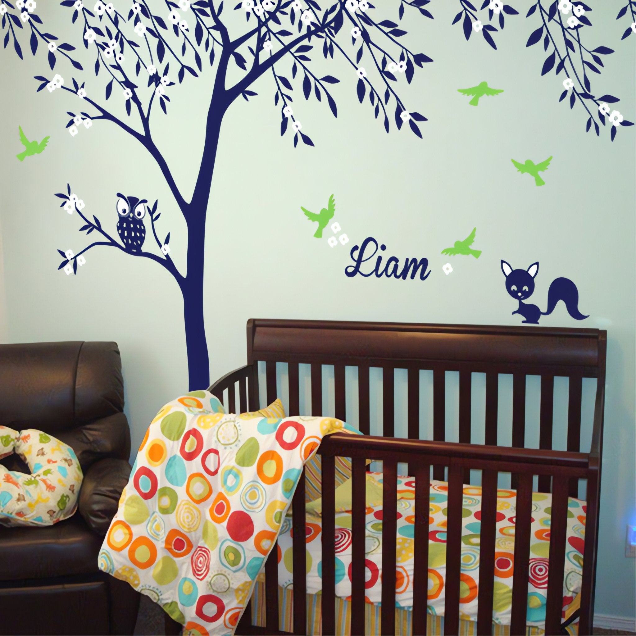 Tree wall sticker with birds, an owl, a squirrel and the name of a loved one in a nursery above a crib.