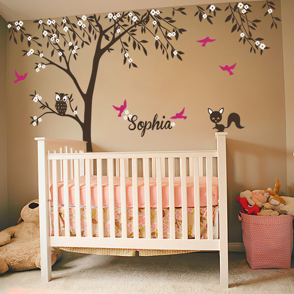 Tree wall sticker with birds, an owl, a squirrel and the name of a loved one in a nursery above a crib.
