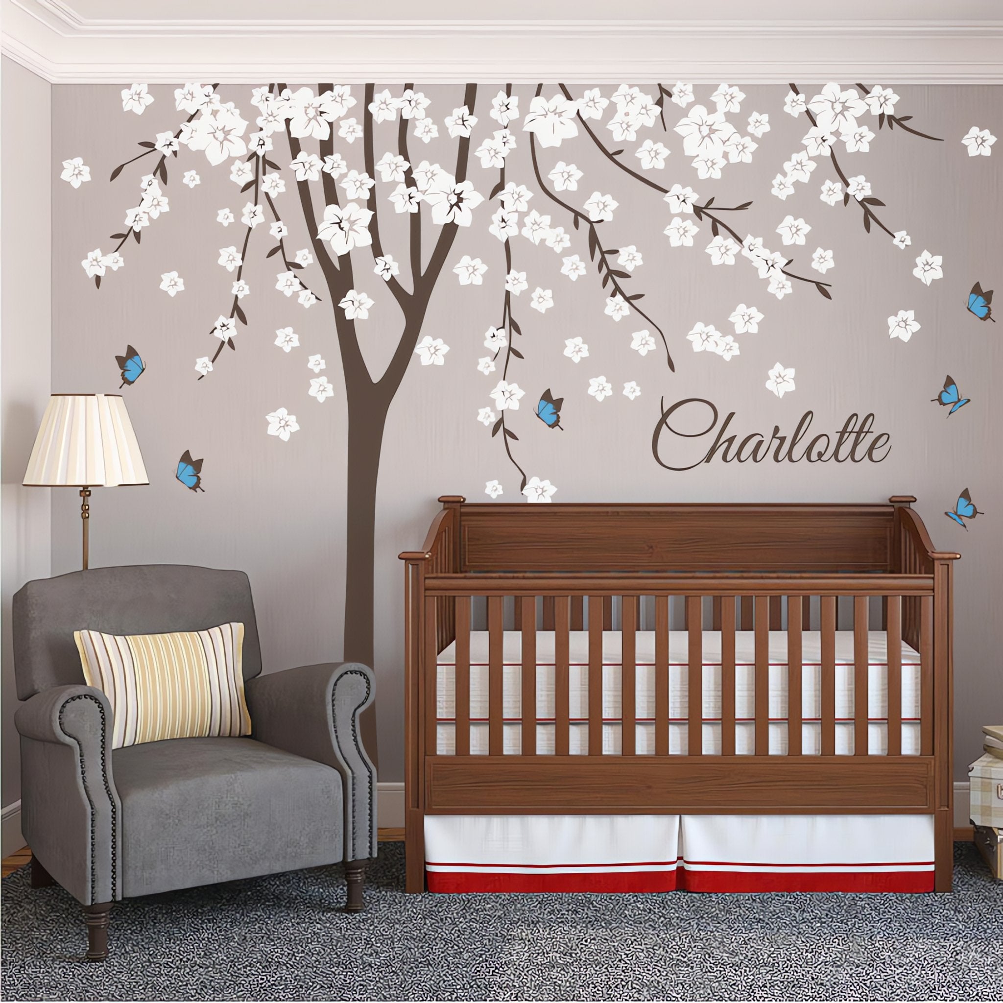 Tree wall sticker with blossoming leaves, butterflies and the name of a loved one in a nursery with a crib and an armchair.