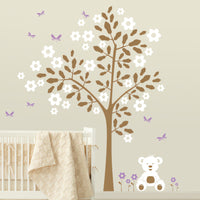 Tree wall sticker with butterflies and a teddy bear in a nursery with a crib.
