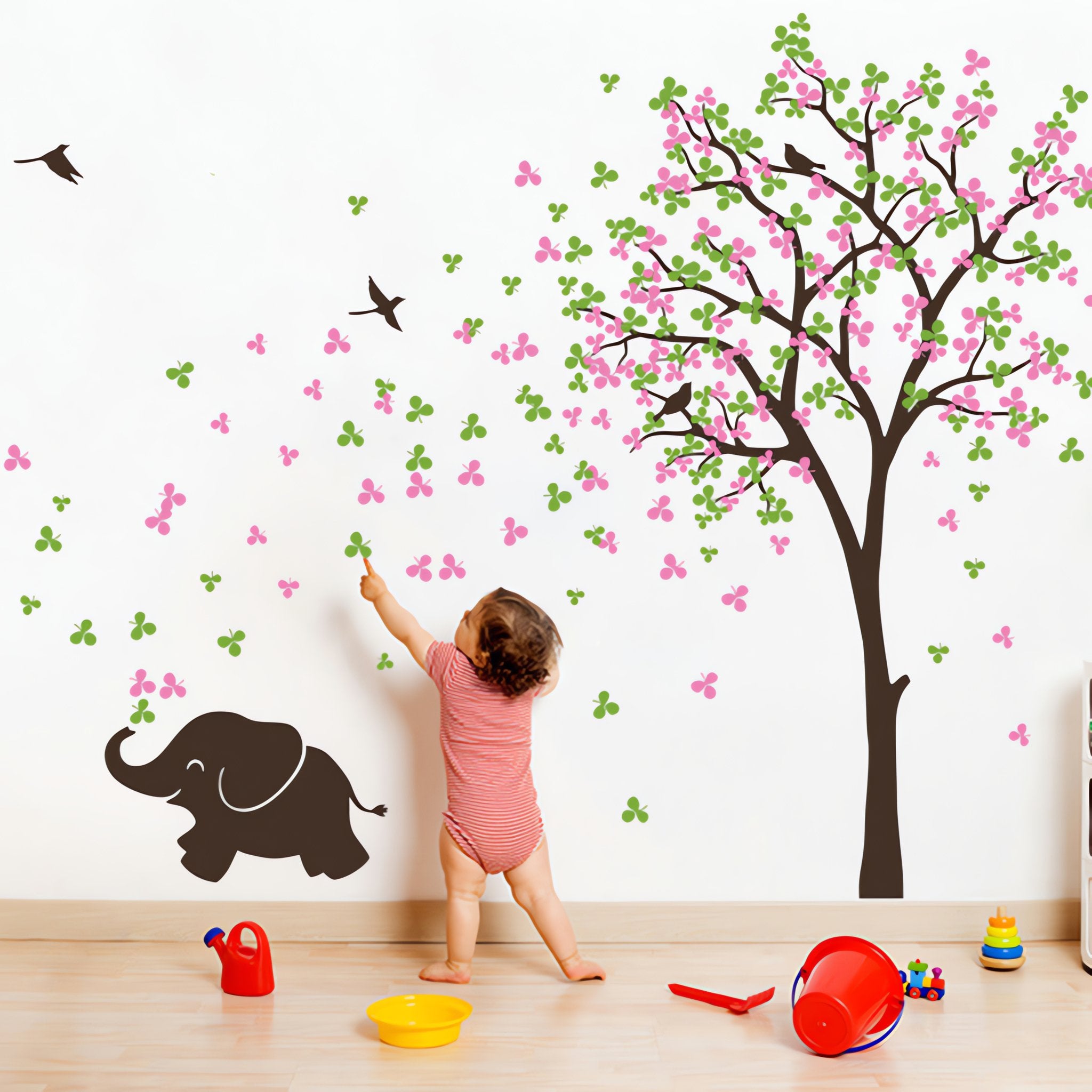 Tree wall sticker with a baby elephant and birds in a nursery with a baby playing and toys.