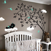 Swaying tree wall sticker with a sleeping bear on a cloud and birds in a nursery with a crib.