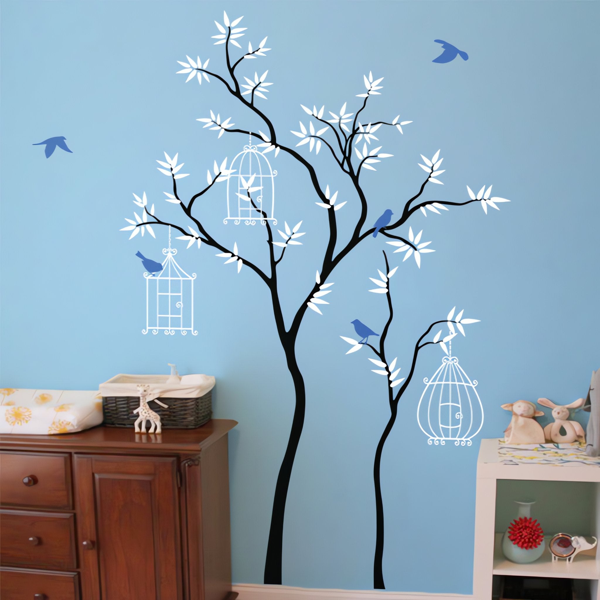 Tree wall sticker with birds and birdcages in a bedroom next to a dresser and shelf.