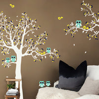 Tree wall sticker with birds, an owl and a hanging branch on the right in a living area with a sofa.