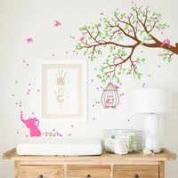 Tree wall sticker with birds, a birdcage, an elephant and a hanging branch on the side next to a framed print and a above a dresser.