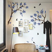 Tree wall sticker with side branches and birds in a room next to a hanging dress, framed pictures and seating.