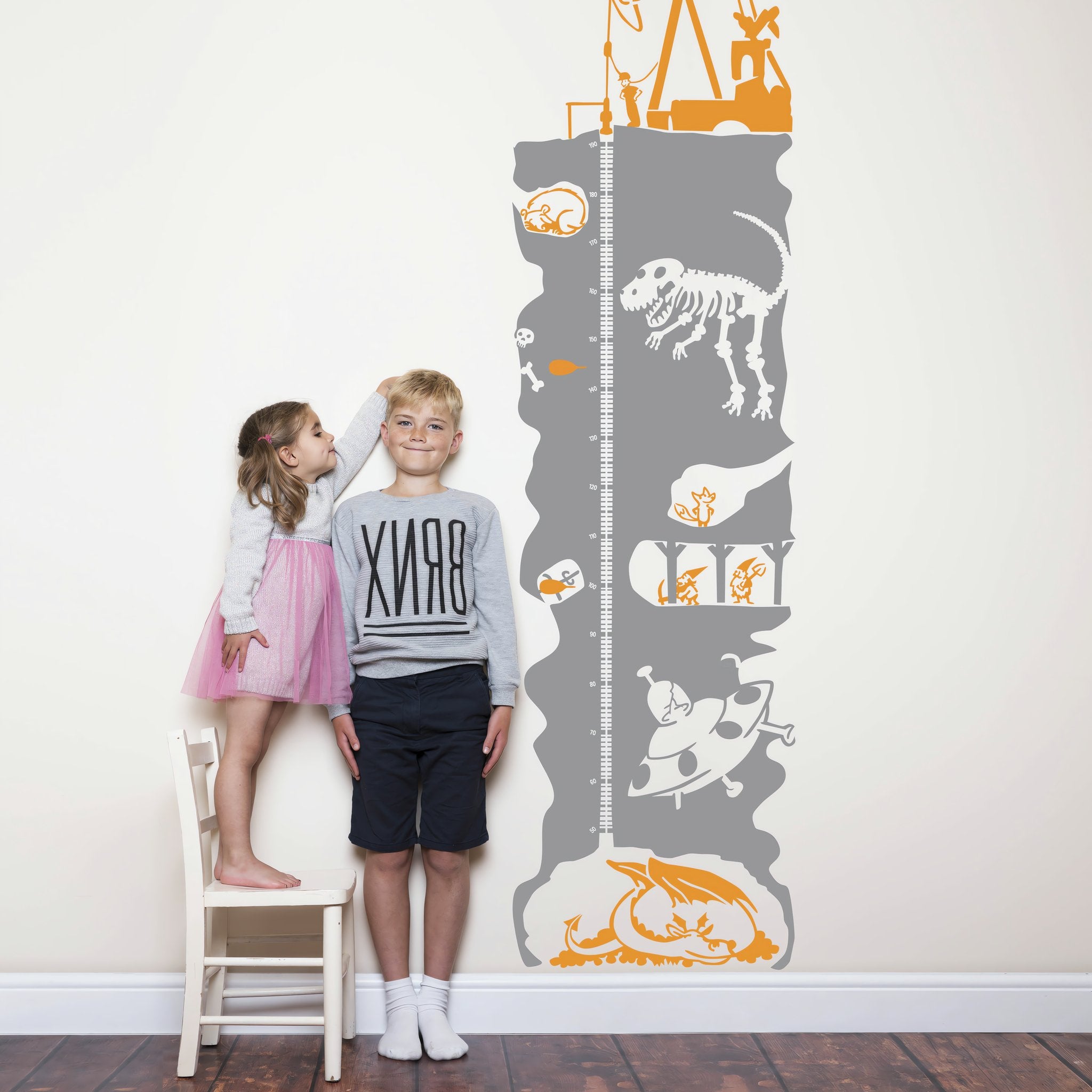 Height chart wall sticker of an underground mineshaft with a young boy and girl nearby.