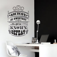 Wall quote sticker with text "Victory Is Sweetest When You've Known Defeat" in an office with a desk and chair.