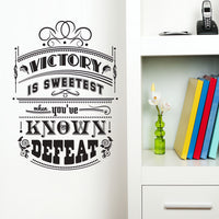 Wall quote sticker with text "Victory Is Sweetest When You've Known Defeat" next to a shelf.