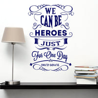 Wall quote sticker with text "We Can Be Heroes Just For One Day" by David Bowie next to a shelf with a lamp and books.