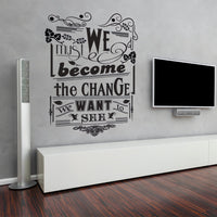 Wall quote sticker with text "We Must Become the Change We Want to See" in a living room next to a flat screen TV.