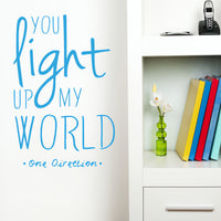 Wall quote sticker with text "You Light Up My World" by One Direction next to a shelf.